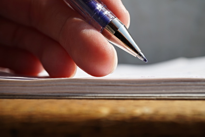 Male hand holding a sharp blue office pen and writing to the white lined notepad as a symbol of taking notes or business communication